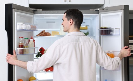 Happy man near refrigerator in kitchen at home, back view