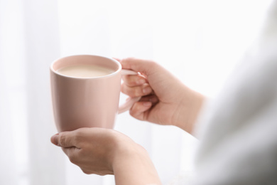 Photo of Woman with cup of hot drink near window at home in morning, closeup