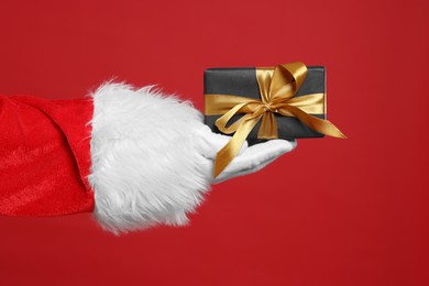 Photo of Santa Claus holding Christmas gift on red background, closeup