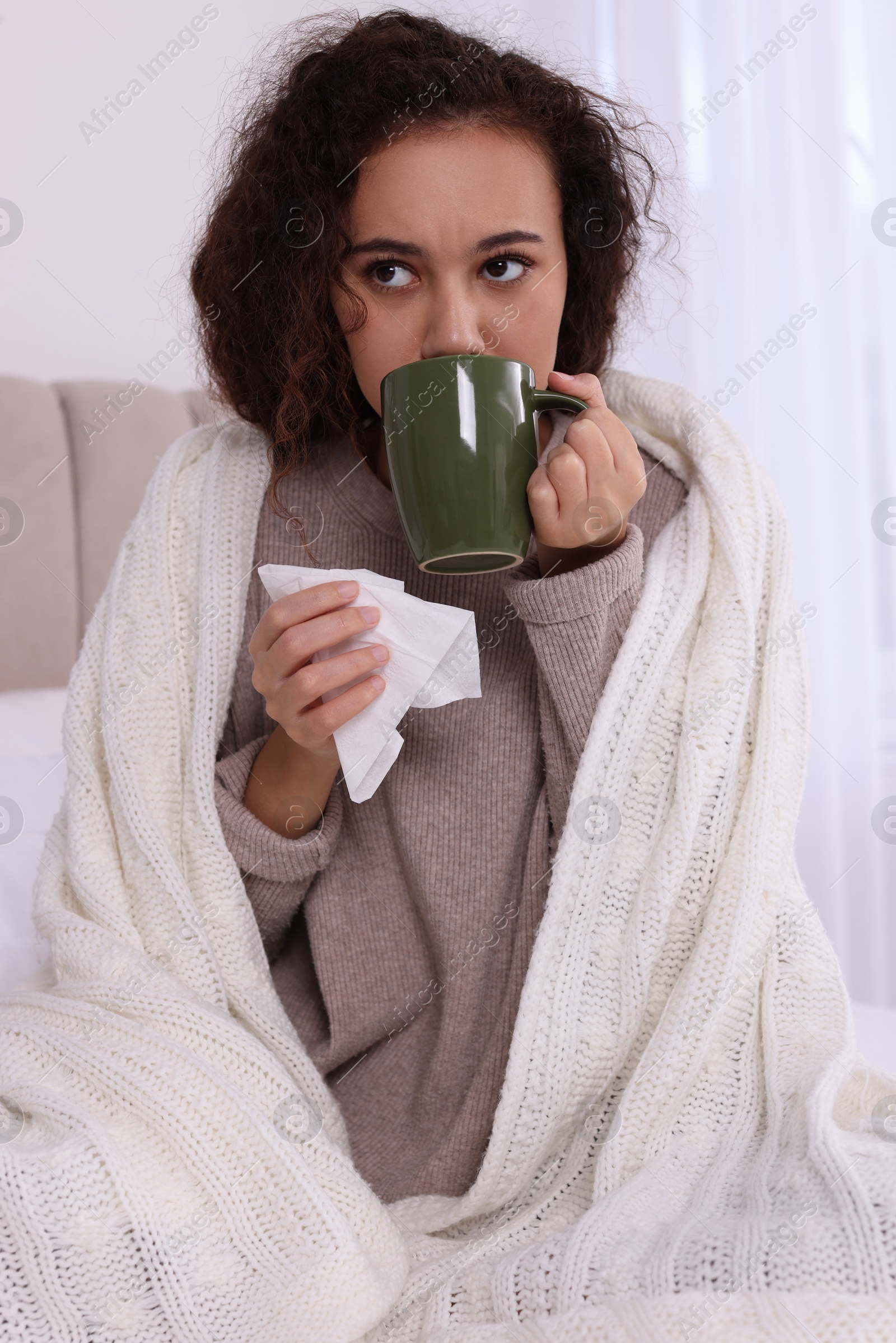 Photo of Sick African American woman with tissue and cup of drink in bed at home