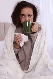 Sick African American woman with tissue and cup of drink in bed at home