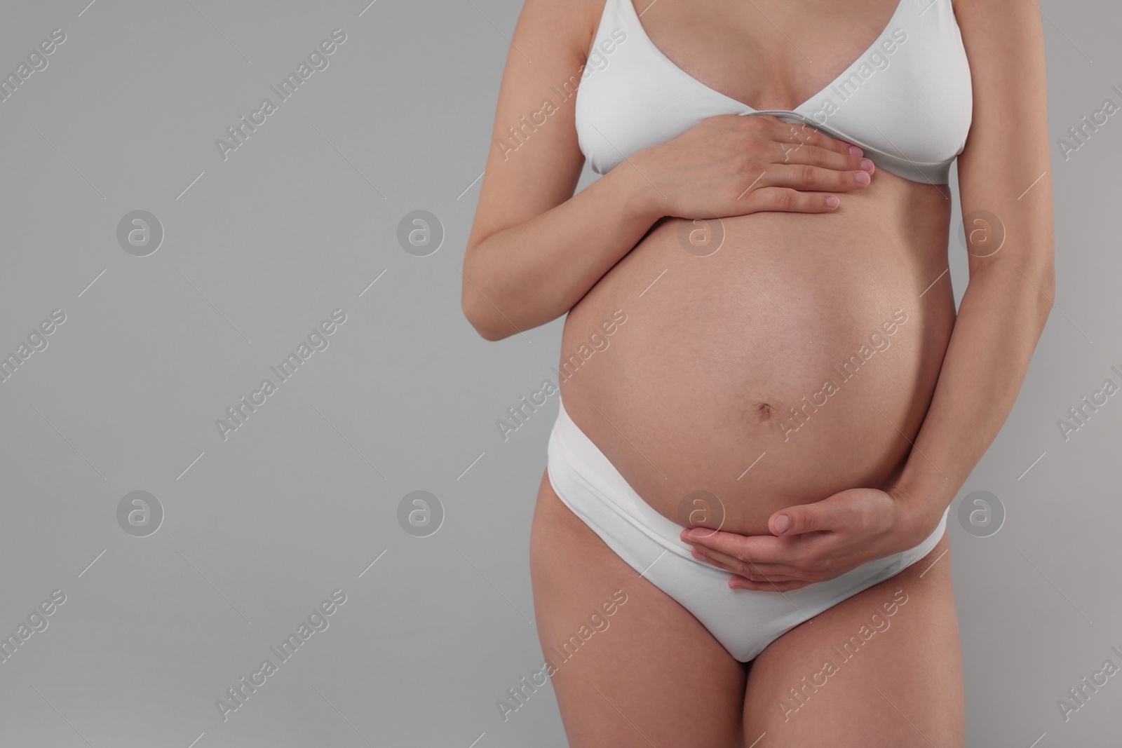 Photo of Pregnant woman in stylish comfortable underwear on grey background, closeup. Space for text