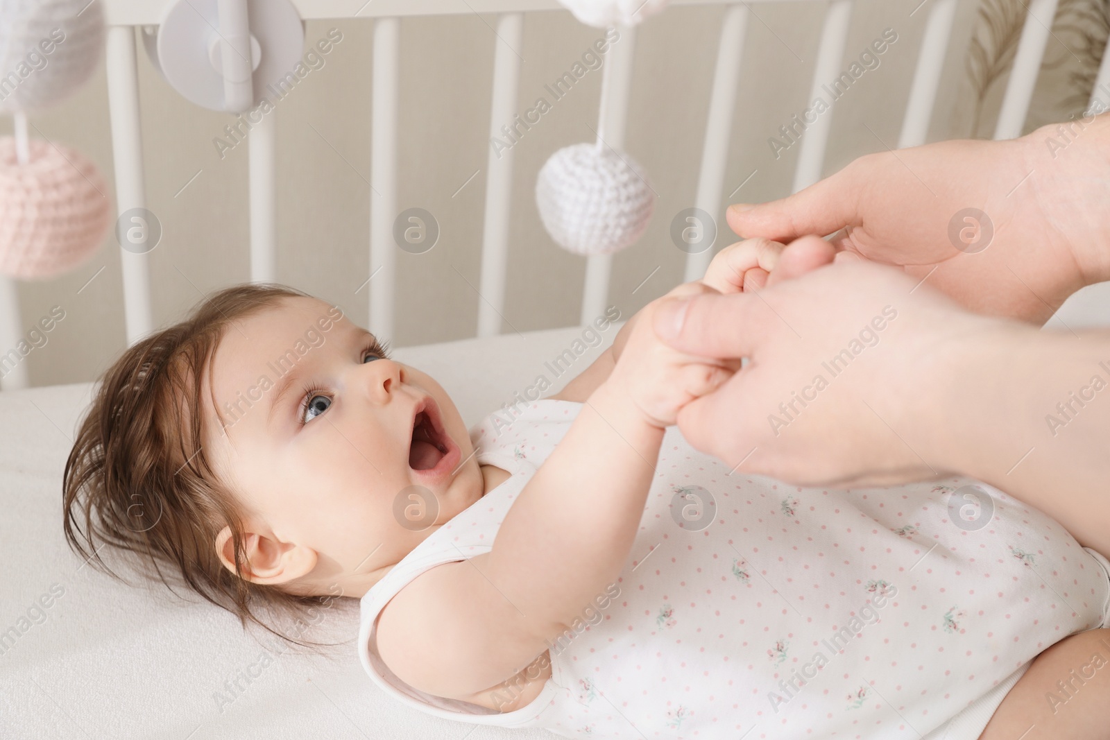 Photo of Father holding baby's hands in crib at home, closeup