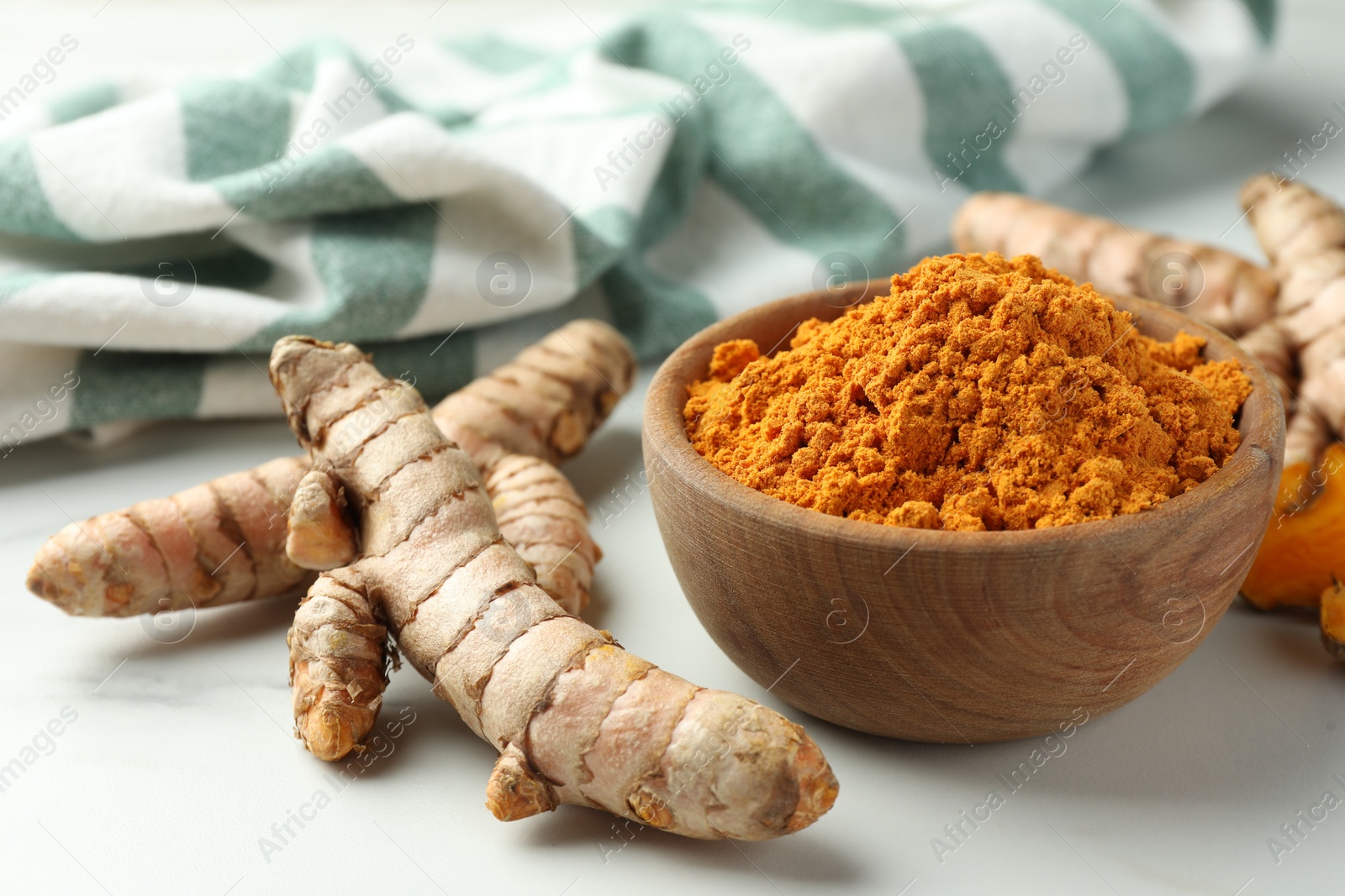 Photo of Aromatic turmeric powder and raw roots on white table, closeup