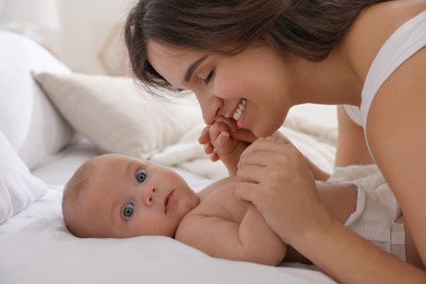 Happy young mother with her cute baby on bed indoors