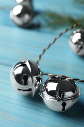 Photo of Silver sleigh bells on light blue wooden background, closeup