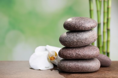 Photo of Stacked spa stones and orchid flower on wooden table against bamboo stems. Space for text
