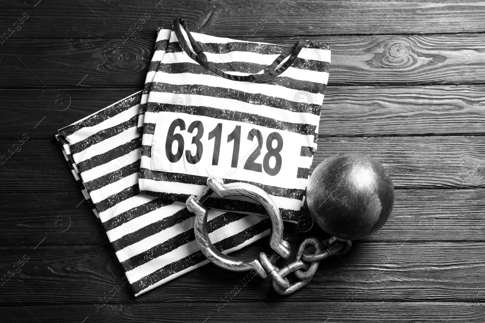 Photo of Prisoner ball with chain and jail clothes on black wooden table, flat lay