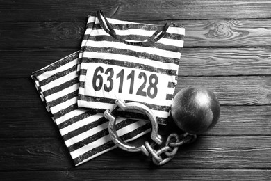 Prisoner ball with chain and jail clothes on black wooden table, flat lay