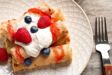 Photo of Thin pancakes served with syrup, cream and berries on plate, closeup