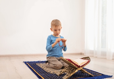 Photo of Little Muslim boy with misbaha and Koran praying on rug indoors