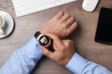 Businessman checking home security system via smartwatch app at office table, top view. Image of room through CCTV camera on display