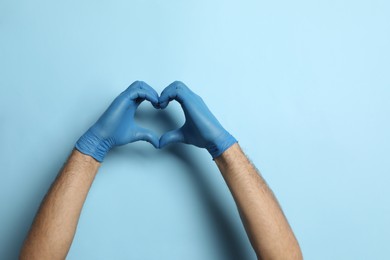 Photo of Doctor in medical gloves making heart with hands on light blue background, closeup. Space for text