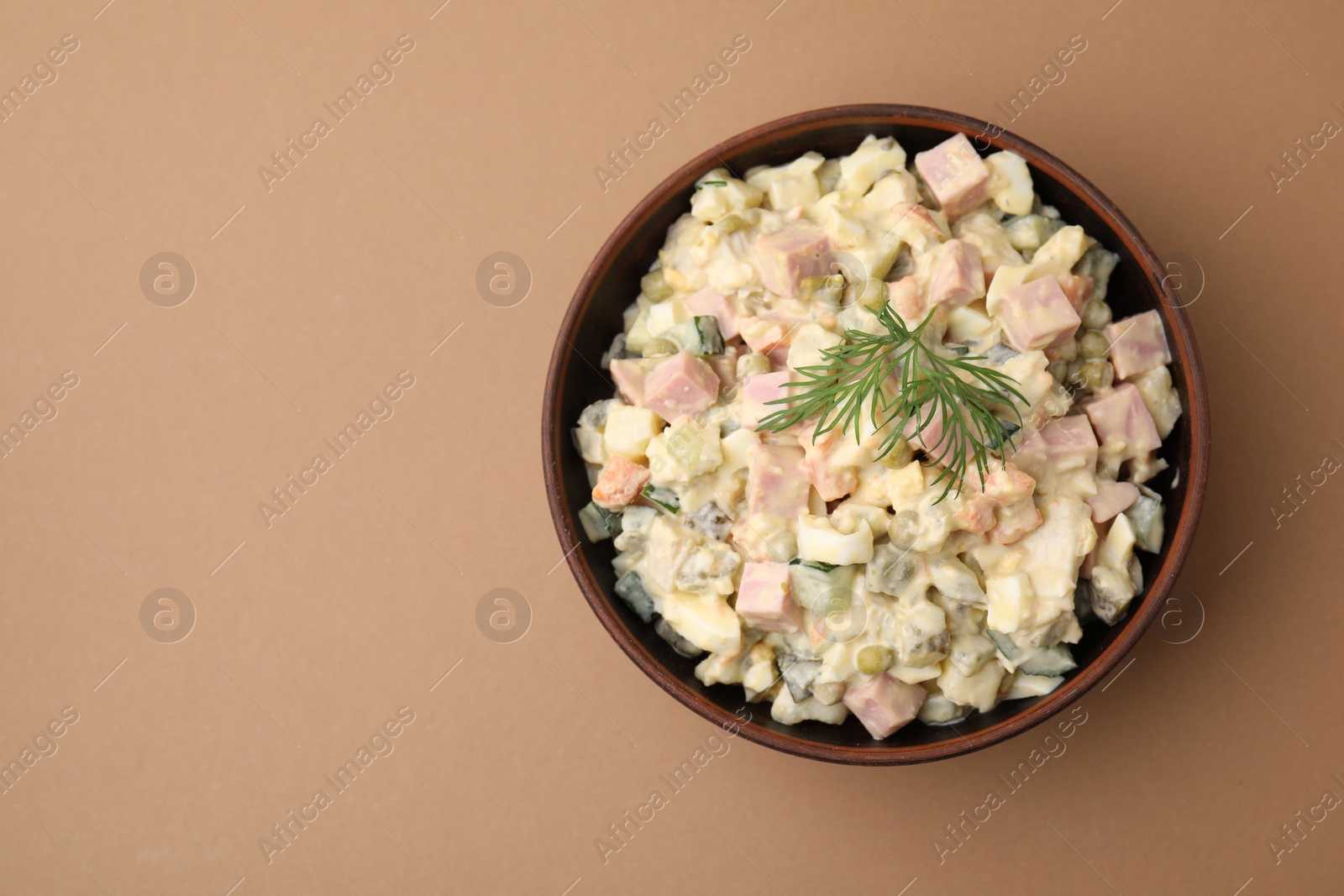 Photo of Tasty Olivier salad with boiled sausage in bowl on beige table, top view. Space for text