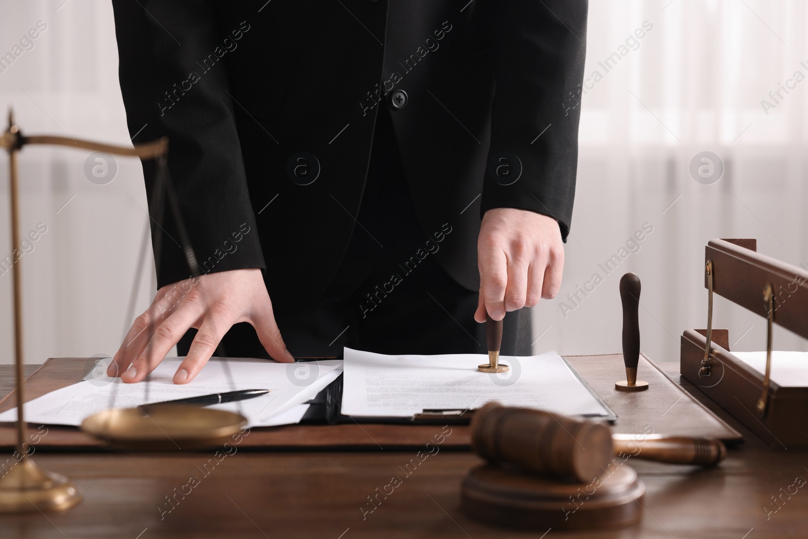 Photo of Notary stamping document at wooden table in office, closeup