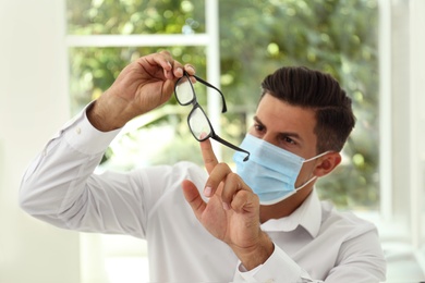 Photo of Man wiping foggy glasses caused by wearing medical mask indoors