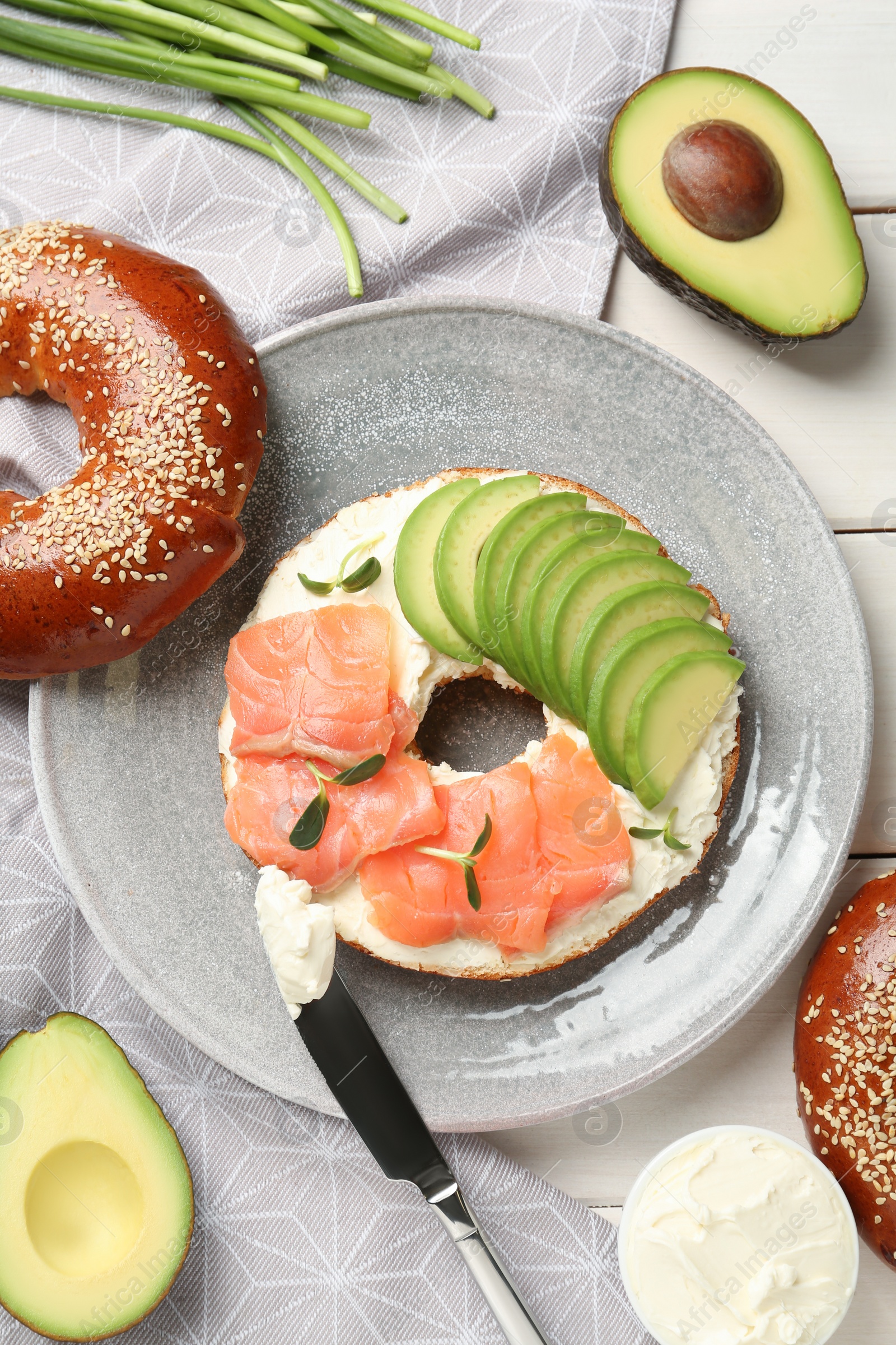 Photo of Delicious bagel with cream cheese, salmon and avocado on table, flat lay