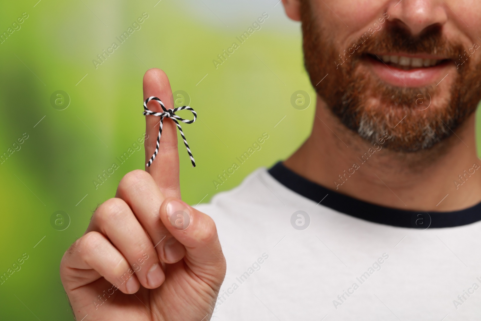 Photo of Man showing index finger with tied bow as reminder on green blurred background, closeup