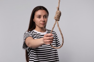 Depressed woman with rope noose on light grey background