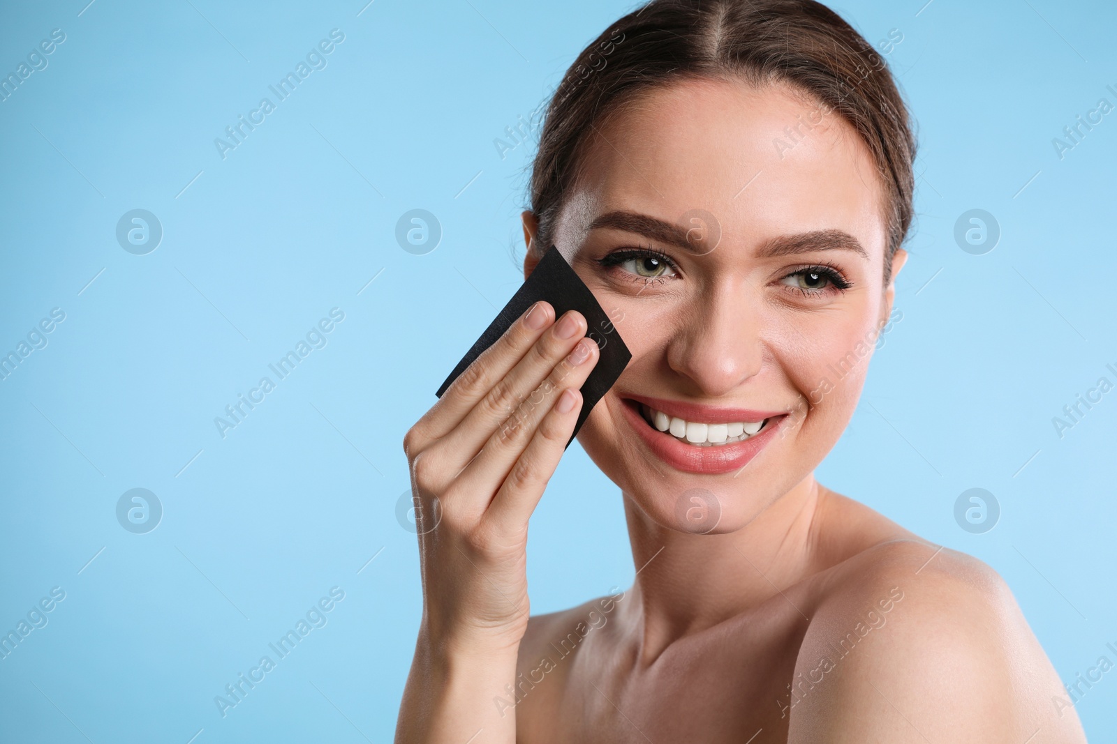 Photo of Beautiful woman using mattifying wipe on light blue background, space for text