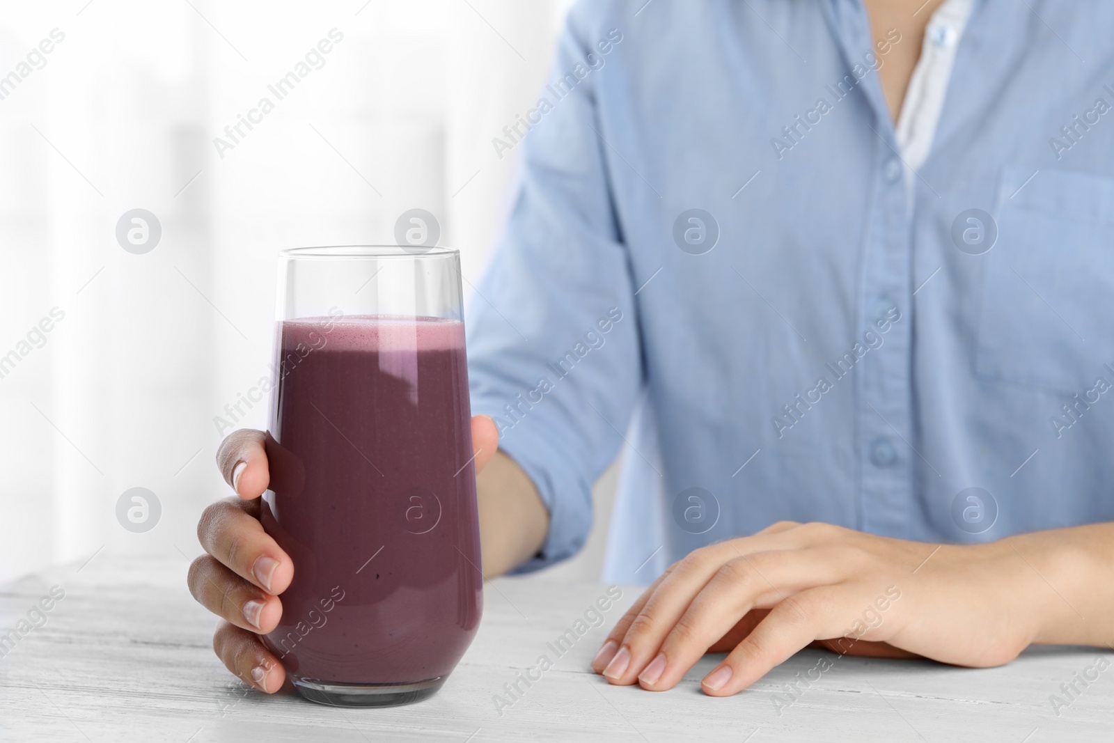 Photo of Woman with glass of fresh acai drink at white wooden table, closeup