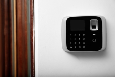 Photo of Modern alarm system with fingerprint scanner on white wall indoors. Space for text