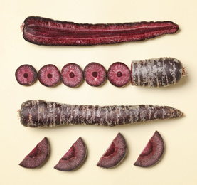 Photo of Whole and cut raw purple carrots on beige background, flat lay