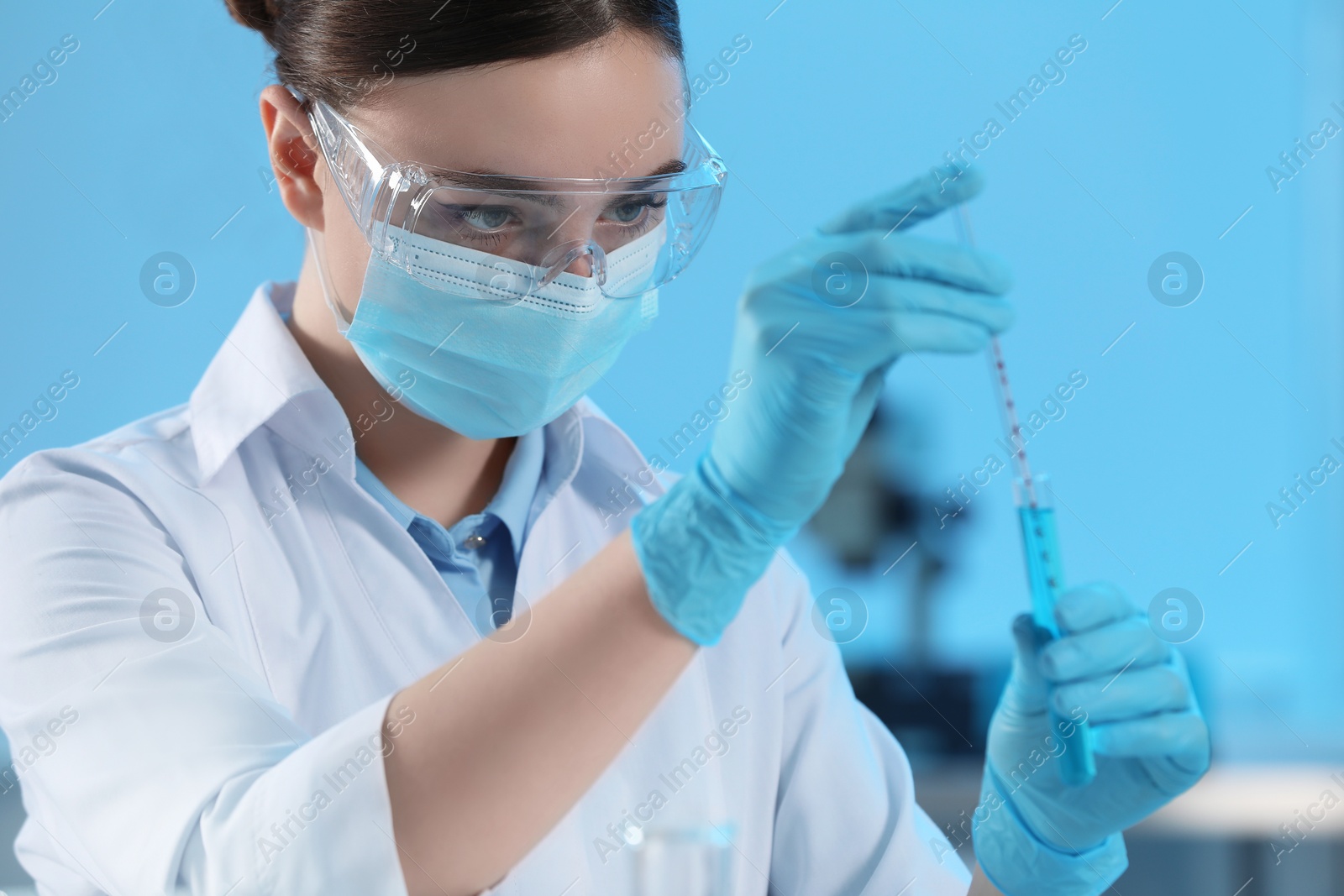 Photo of Scientist taking sample of light blue liquid in laboratory