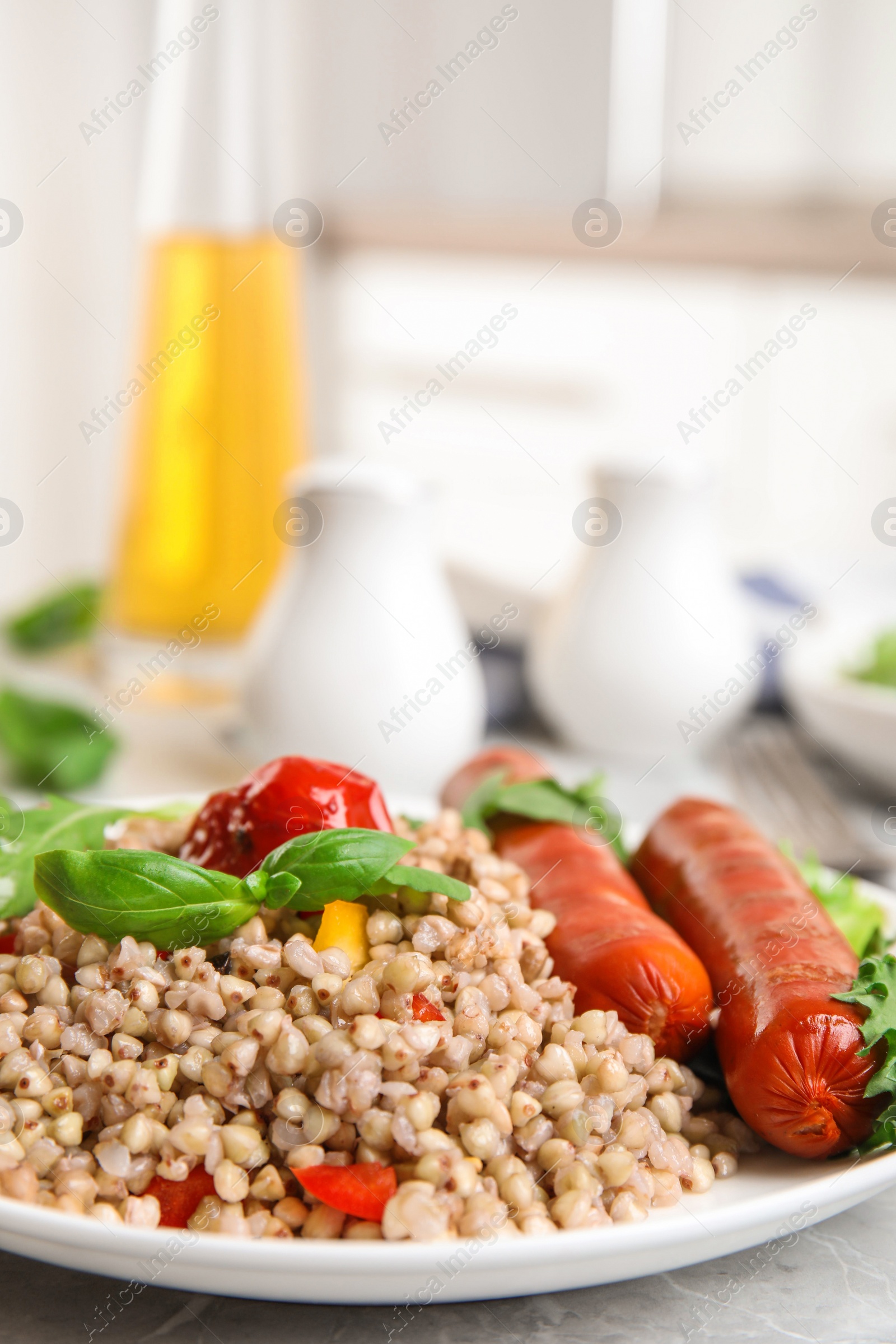 Photo of Tasty buckwheat porridge with sausages and vegetables on light grey marble table indoors, closeup. Space for text