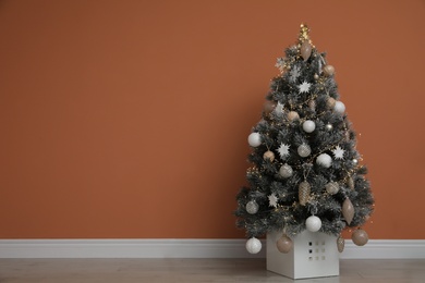 Photo of Beautiful decorated Christmas tree near orange wall indoors, space for text