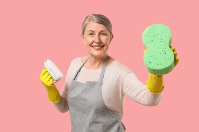 Photo of Happy housewife with sponge and brush on pink background