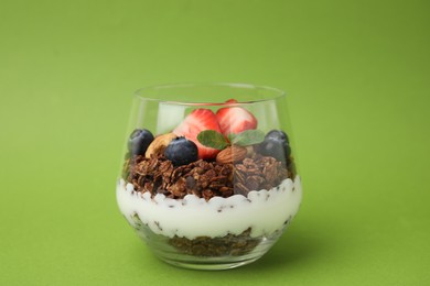 Photo of Tasty granola with berries, nuts and yogurt in glass on green background