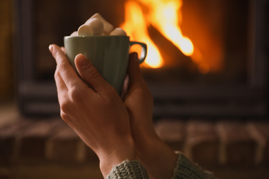 Photo of Woman with cup of sweet cocoa near fireplace indoors, closeup