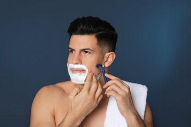 Photo of Handsome man shaving with razor on blue background