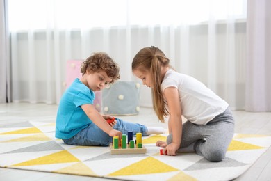 Cute little children playing with set of wooden geometric figures on floor in kindergarten