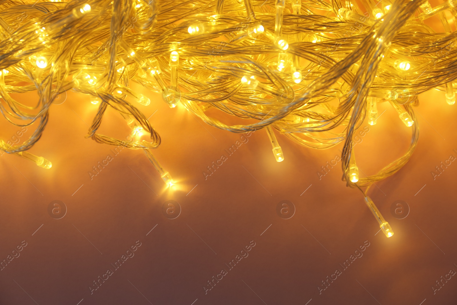 Photo of Glowing Christmas lights on violet background, top view