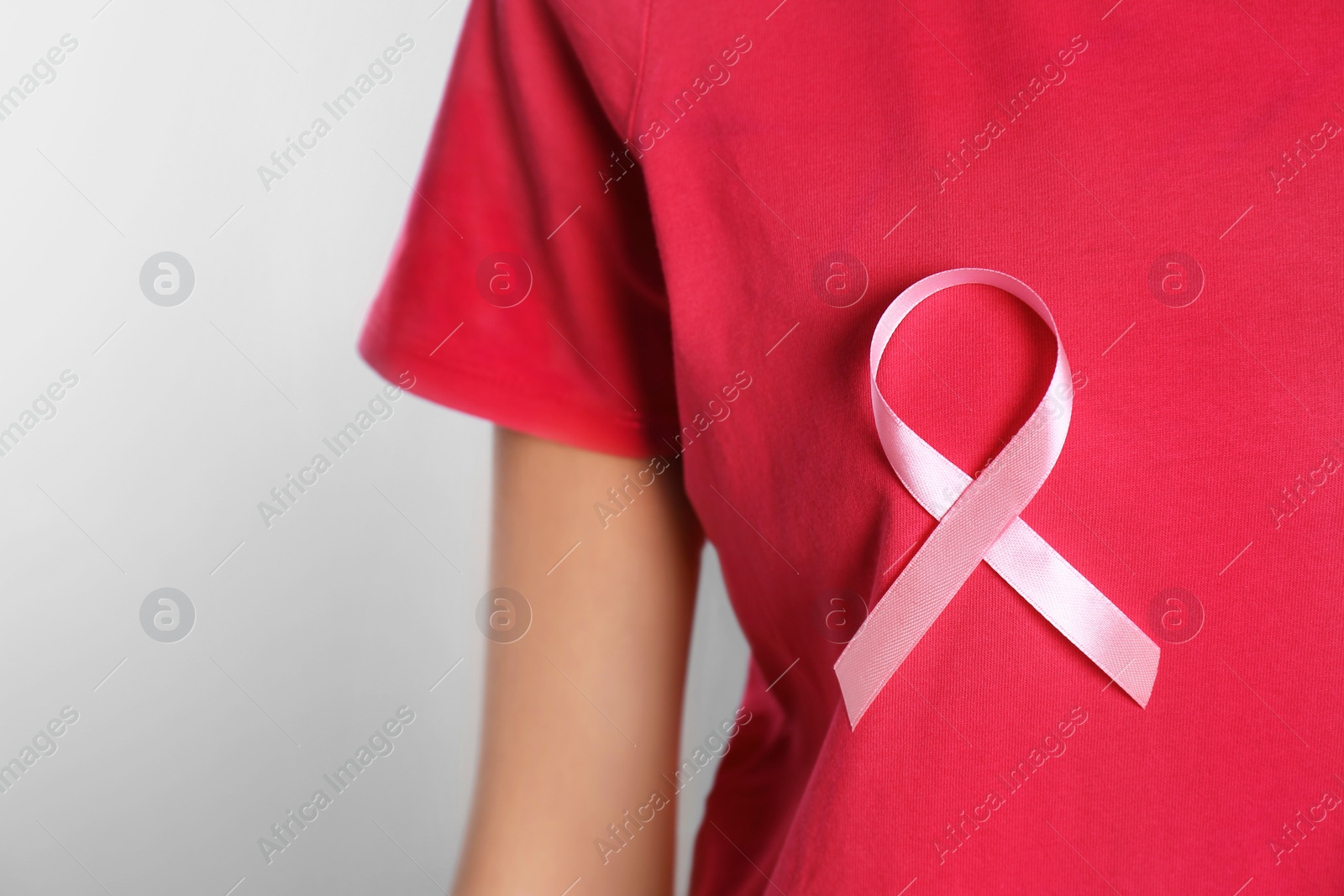 Photo of Woman with pink ribbon on light background, closeup with space for text. Breast cancer awareness