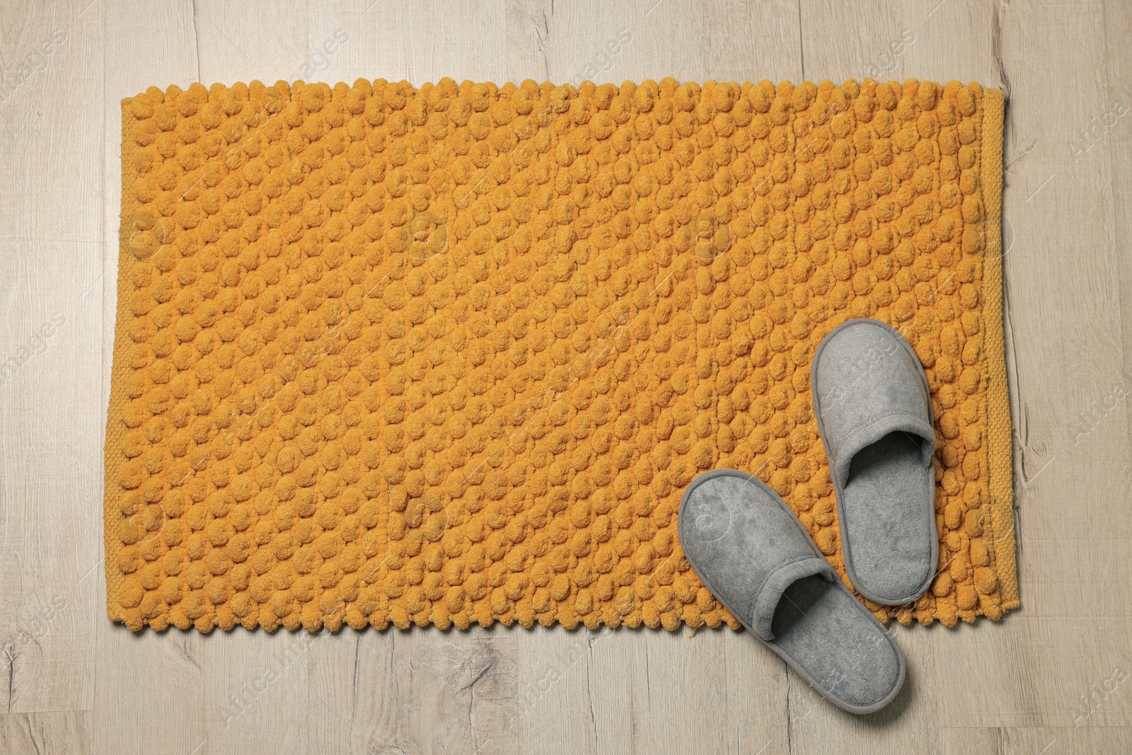 Photo of Soft orange bath mat and slippers on floor, top view