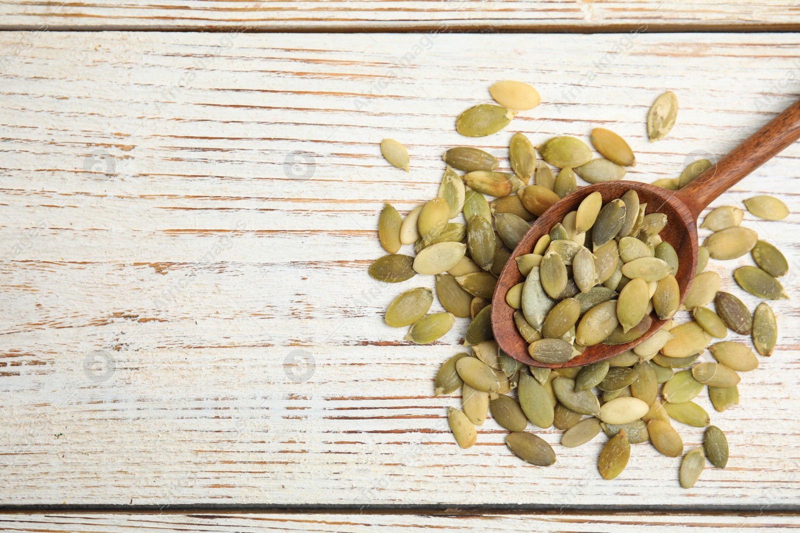 Photo of Spoon with pumpkin seeds on white wooden table, flat lay. Space for text