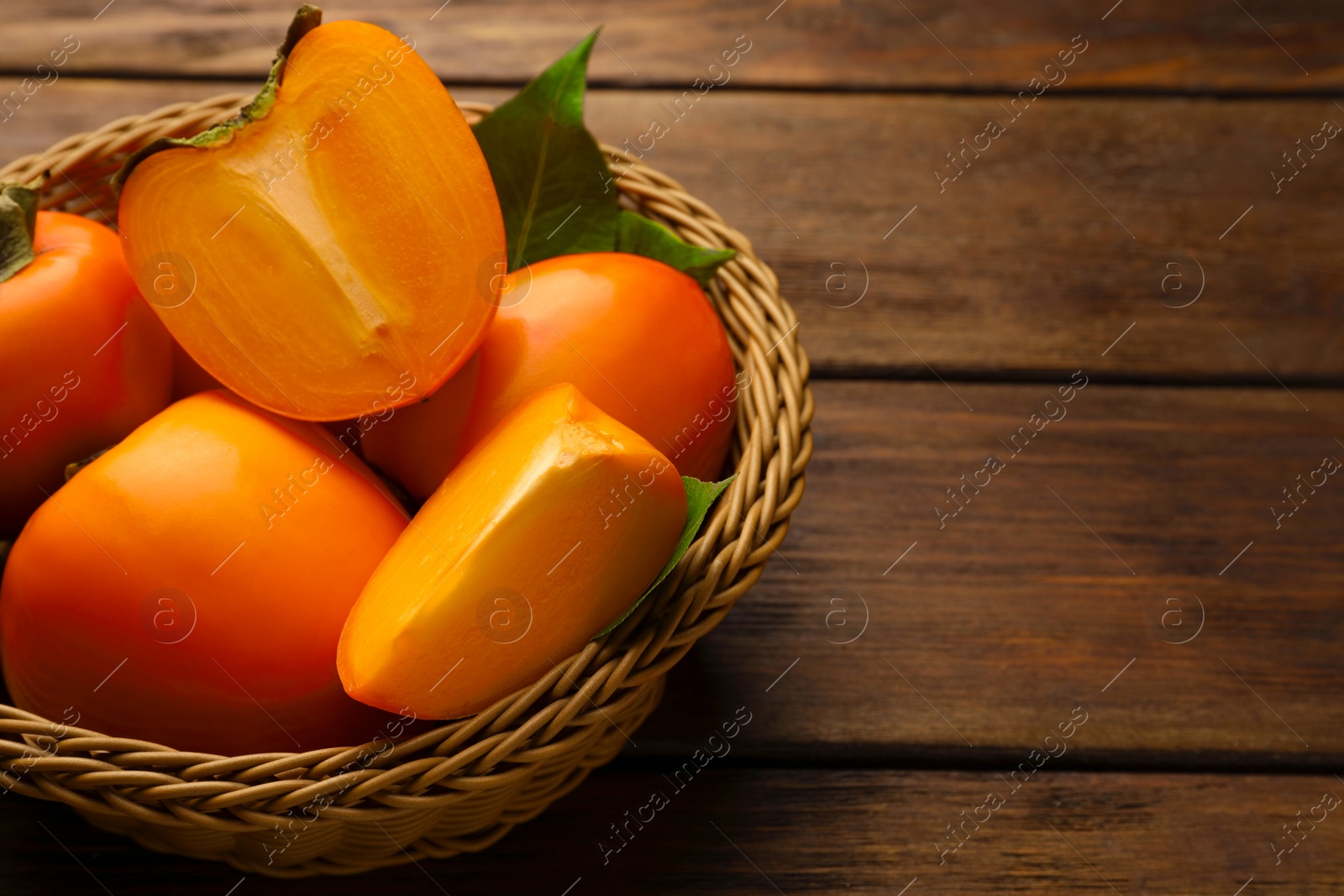 Photo of Delicious ripe persimmons in wicker basket on wooden table, space for text