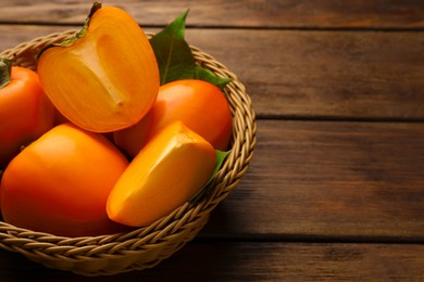 Photo of Delicious ripe persimmons in wicker basket on wooden table, space for text