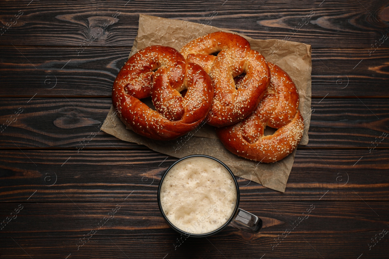 Photo of Tasty freshly baked pretzels and mug of beer on wooden table, flat lay