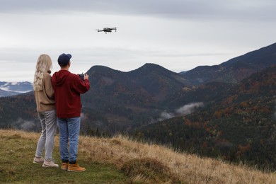 Photo of Young couple operating modern drone with remote control in mountains, back view. Space for text