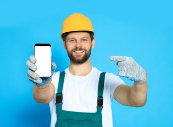 Photo of Professional repairman in uniform showing smartphone against light blue background, focus on screen