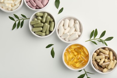 Photo of Different vitamin capsules in bowls and leaves on white background, flat lay. Space for text