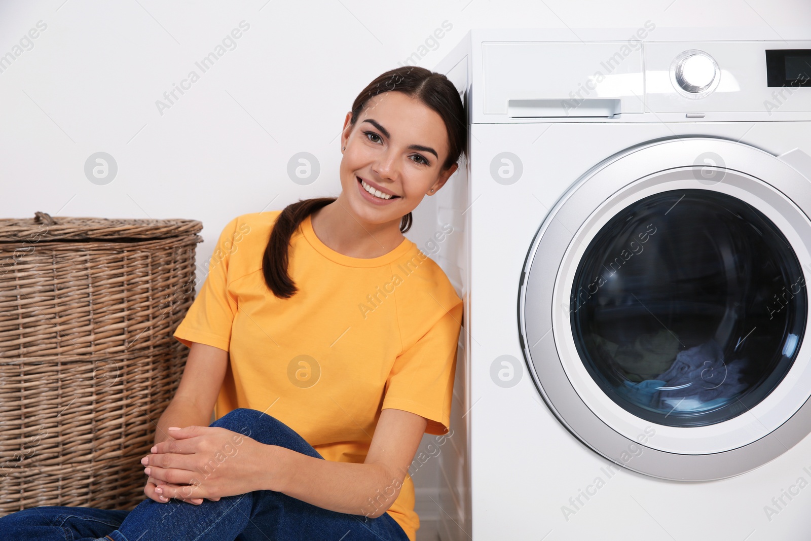 Photo of Young woman near washing machine at home. Laundry day