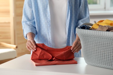 Photo of Woman folding clean laundry at white table indoors, closeup