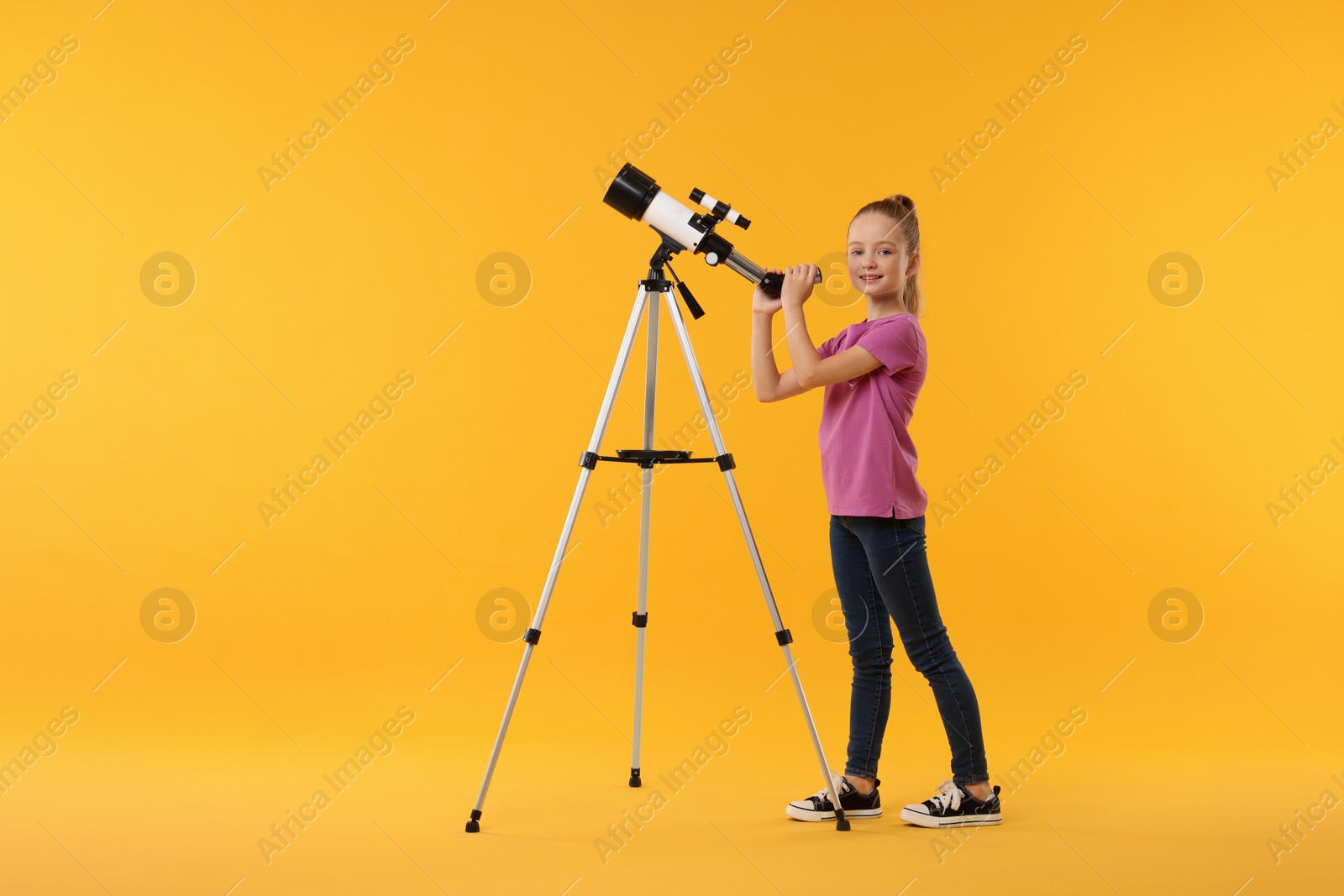 Photo of Happy little girl with telescope on orange background