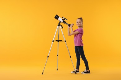 Happy little girl with telescope on orange background