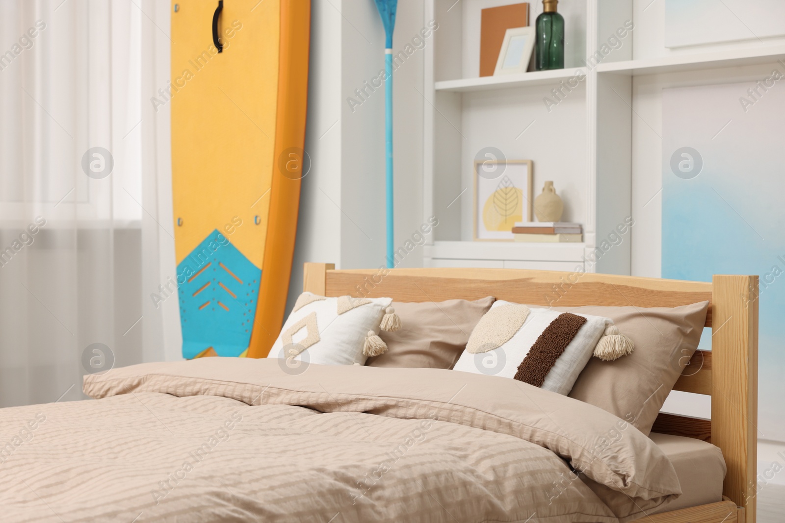 Photo of SUP board, bed and furniture in room. Interior design